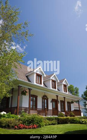 Réplique de l'ancienne maison en stuc blanc de style cottage Canadiana 1860s avec garniture en bois teinté brun et cour avant paysagée en été. Banque D'Images