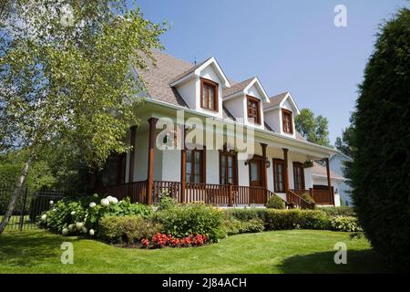 Réplique de l'ancienne maison en stuc blanc de style cottage Canadiana 1860s avec garniture en bois teinté brun et cour avant paysagée en été. Banque D'Images