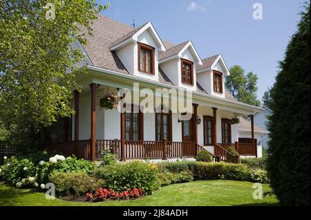 Réplique de l'ancienne maison en stuc blanc de style cottage Canadiana 1860s avec garniture en bois teinté brun et cour avant paysagée en été. Banque D'Images