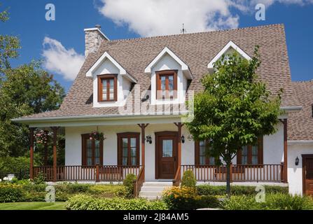 Réplique de l'ancienne maison en stuc blanc de style cottage Canadiana de 1860s avec garniture en bois teinté brun et jardin paysagé de cour avant en été. Banque D'Images