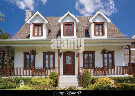 Réplique de l'ancienne maison en stuc blanc de style cottage Canadiana de 1860s avec garniture en bois teinté brun et jardin paysagé de cour avant en été. Banque D'Images