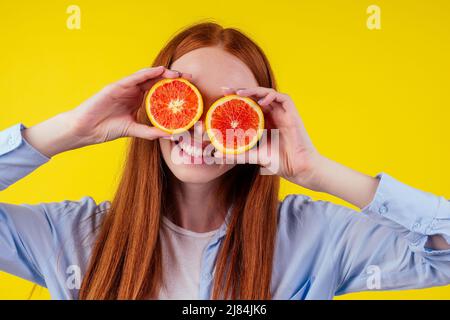 gaie, femme au gingembre rougeâtre tenant l'orenge rouge dans le fond jaune studio, concept d'immunité aux vitamines d'automne Banque D'Images