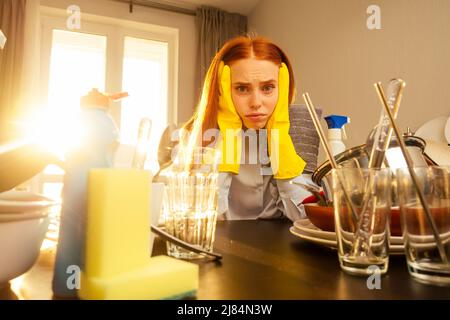 malheureux gingembre rougeâtre belle femme portant le gant jaune et la pile de lavage montagnes de plats sales: tasses, poêle, casserole dans la cuisine Banque D'Images