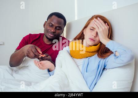 Malade ensemble. Jeune homme hispanique et jeune femme au gingembre à poil rouge éternuant dans des serviettes en papier au lit Banque D'Images