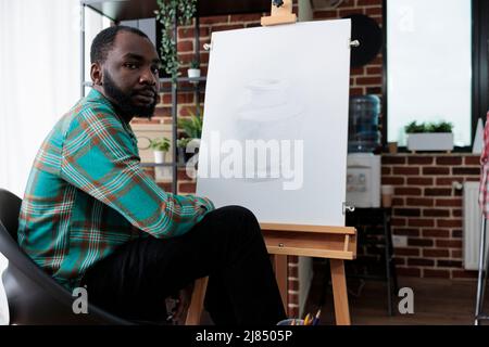 Portrait d'un jeune peintre assis devant un vase d'esquisse en toile blanche à l'aide d'un crayon graphique pendant la leçon d'art en studio de créativité. Artiste souriant développant des compétences artistiques pour la croissance personnelle Banque D'Images