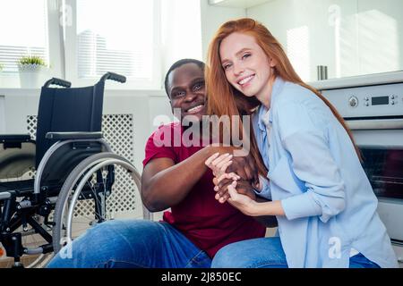 Jeune homme afro-américain handicapé barbu en fauteuil roulant et sa jolie femme au kichen Banque D'Images