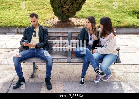 Deux amis assis sur un banc à côté d'un garçon inconnu. Photo de haute qualité Banque D'Images