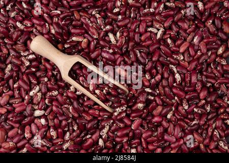 haricots rouges dans une pelle en bois sur le fond de beaucoup de grains de haricots secs vue du dessus, texture des haricots rouges, fond de nourriture gros plan Banque D'Images