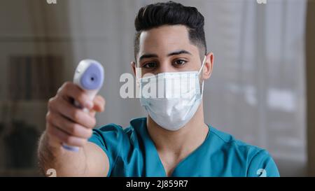 Homme arabe travailleur médical médecin chirurgien homme en masque de protection prenant de la température avec un thermomètre numérique infrarouge sans contact pendant le Covid-19 Banque D'Images