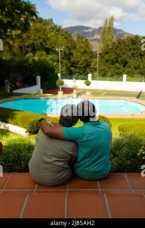 Vue arrière de l'homme aîné biracial avec la main sur l'épaule de la femme regardant la vue tout en étant assis sur des marches Banque D'Images