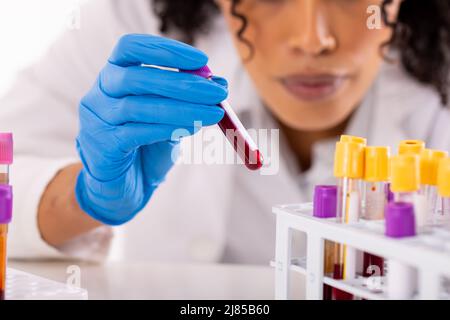 Section médiane de la femme afro-américaine de l'adulte moyen médecin plaçant les tubes à essai dans le plateau sur la table Banque D'Images