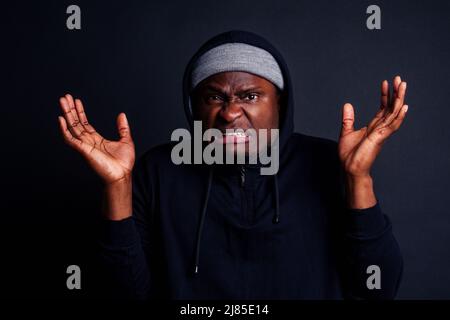 inquiet jeune afro-américain mele portant un chapeau gris et un sweat à capuche noir se cachant du studio de l'attaquant du violeur, le sol noir Banque D'Images