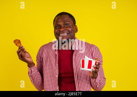 drôle africain américain homme mangeant la jambe de poulet frite dans le fond jaune studio Banque D'Images