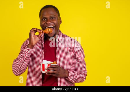 drôle africain américain homme mangeant la jambe de poulet frite dans le fond jaune studio Banque D'Images