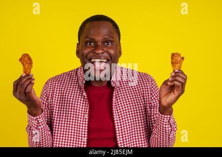 drôle africain américain homme mangeant la jambe de poulet frite dans le fond jaune studio Banque D'Images