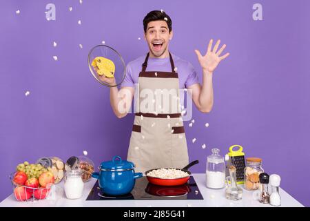 Photo de joli choqué mec porter tablier gris ouvert poêle pop maïs explosion isolé couleur violet fond Banque D'Images