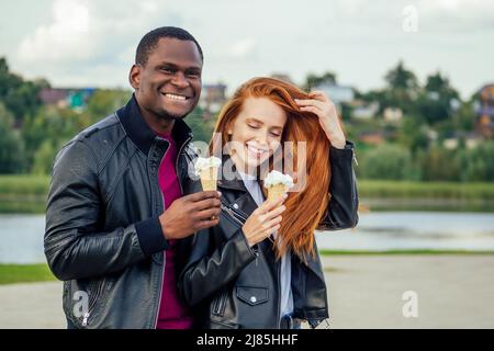 Couple multi-ethnique divers manger de la crème glacée dans le parc d'automne de printemps Banque D'Images