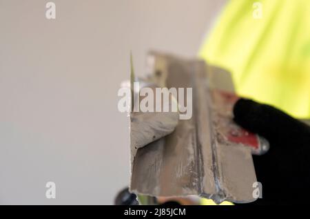 Le constructeur avec une spatule dans ses mains agite le mélange de plâtre sur une spatule, gros plan. Banque D'Images