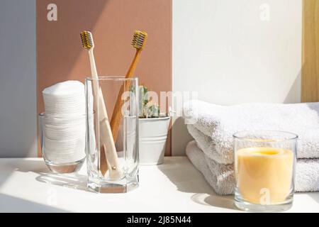 Salle de bains, brosses à dents dans un verre sur lequel tombent les rayons du soleil, serviettes en coton blanc, cactus verts, produits d'hygiène personnelle. Banque D'Images