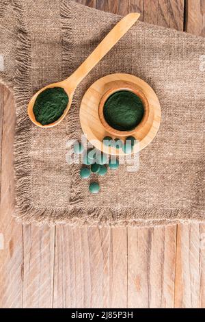 Poudre de spiruline verte et comprimés d'algues dans une cuillère en bois écologique et un bol sur le jute. Fond en bois vertical. Superfood Banque D'Images