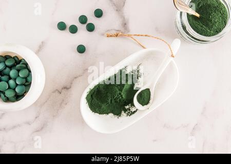 Poudre de spiruline verte biologique et comprimés d'algues vertes dans un bol blanc et une cuillère sur une table en marbre. Vue du dessus. Source alimentaire de protéines vitaminées Banque D'Images