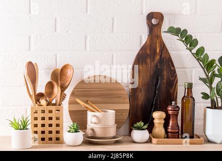 Divers types d'ustensiles de cuisine, planches en bois, récipients à épices, plante en pot verte sur un comptoir moderne. Intérieur de cuisine à la mode Banque D'Images