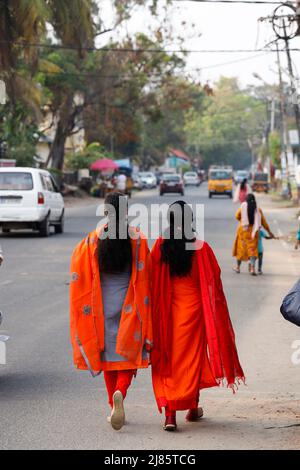 Deux indiennes portant des saris rouges marchant le long de la rue à Tangassery, Thangassery, Kerala, Inde. Banque D'Images