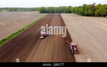 Un agriculteur laboure ses terres agricoles sèches, tandis qu'une autre machine à gauche est occupée à semer des pommes de terre. Banque D'Images