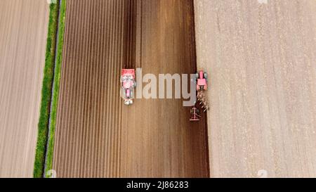 Un agriculteur laboure ses terres agricoles sèches, tandis qu'une autre machine à gauche est occupée à semer des pommes de terre. Banque D'Images