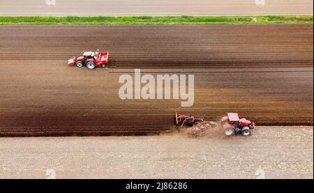 Un agriculteur laboure ses terres agricoles sèches, tandis qu'une autre machine à gauche est occupée à semer des pommes de terre. Banque D'Images