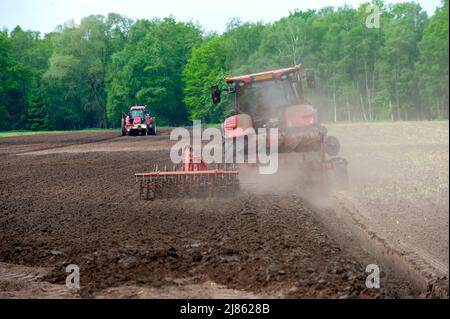Un agriculteur laboure ses terres agricoles sèches, tandis qu'une autre machine à gauche est occupée à semer des pommes de terre. Banque D'Images