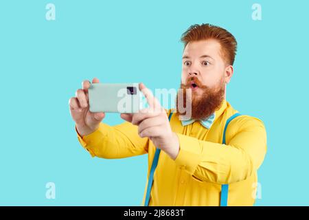 Drôle barbu gros homme isolé sur fond turquoise prend selfie sur son téléphone mobile Banque D'Images