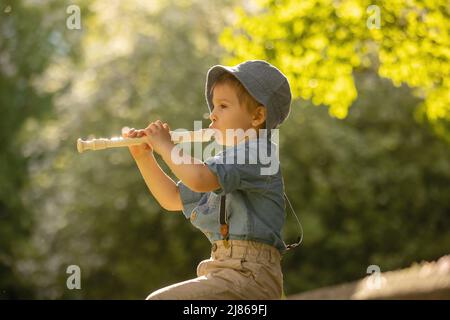 Enfant élégamment habillé, garçon avec chien d'animal, jouant dans le parc sur la flûte, appréciant sa compagnie d'ami d'animal de compagnie Banque D'Images