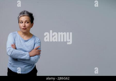 Femme mûre réfléchie avec cheveux gris en 50s posant avec les mains pliées et l'espace de copie sur droite isolée sur fond blanc. Copier l'espace et l'emplacement pour le placement du produit. Une beauté vieillie. Image en tons. Banque D'Images