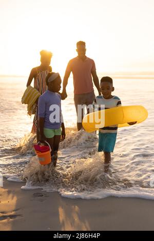 Parents afro-américains regardant son fils et sa fille jouer avec anneau gonflable et seaux en mer Banque D'Images