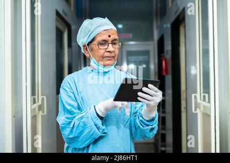 Chirurgien senior dans la blouse d'opération occupé à vérifier le rapport de patient dans le couloir de l'hôpital o tablette - concept de la technologie, dispositif numérique et consultant Banque D'Images