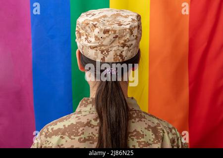 Soldat féminin de l'armée américaine en uniforme de modèle numérique militaire aux États-Unis, regardant le drapeau lgbt. Etats-Unis, uniforme de camouflage, drapeau arc-en-ciel, symbole d'amour dans Banque D'Images