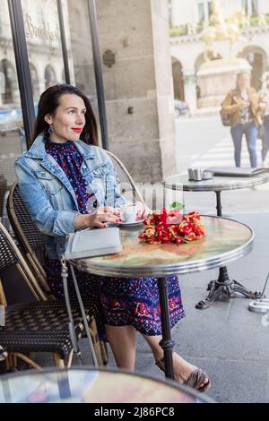 Belle femme avec de longs cheveux de brunette dans la robe bleue assis dans le café de rue Banque D'Images