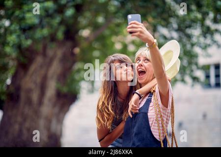 Les jeunes femmes qui font des expressions drôles et goofy visage et prenant le selfie, dans la rue. Jeunes femmes de la ville européenne. Voyage, amusement, concept de l'ensemble. Banque D'Images