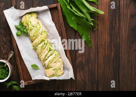 Brioche au pesto d'ail sauvage tressée. Pain frais cru ou non cuit fait maison avec pesto à l'ail sauvage sur une planche en bois sur fond de table en bois. Banque D'Images