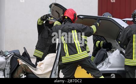 après l'accident de la route, les pompiers retirent le capot de la voiture pour libérer la personne blessée des tôles tordues du véhicule accidenté Banque D'Images