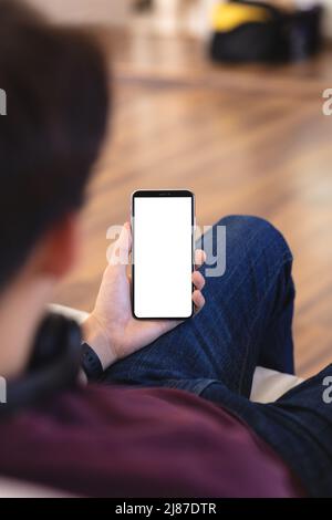 Vue en grand angle d'un adolescent asiatique à l'aide d'un téléphone portable tout en étant assis sur un canapé dans le salon Banque D'Images