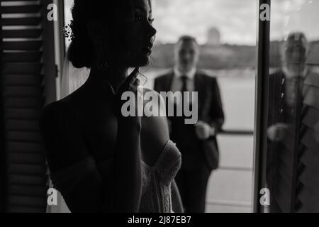 Un groom élégant et une belle mariée brune dans une robe blanche sont debout sur un balcon sur la toile de fond de la rivière. Portrait de mariage, photo Banque D'Images