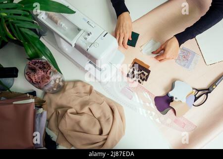 très belle couturière avec de longs cheveux écrit dans un carnet. la tailleur crée une collection de tenues. jeune femme designer vêtements de travail Banque D'Images