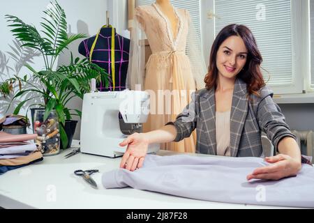 Portrait d'une couturière dans une veste à carreaux travaillant dans son atelier de couture, elle montrant l'intérieur de la doublure de vêtements Banque D'Images