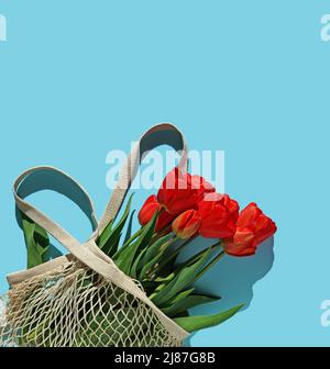 Bouquet de tulipes rouge vif dans un sac à ficelle blanche sur fond bleu. Conception de félicitations et un cadeau. Flat lay, vue de dessus. Banque D'Images