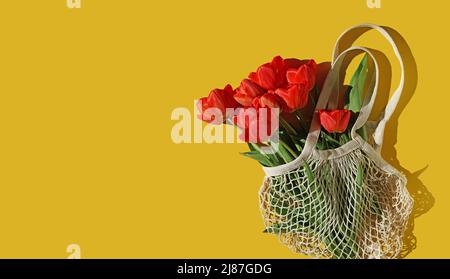 Bouquet de tulipes rouge vif dans un sac à ficelle blanche sur fond jaune. Conception de félicitations et un cadeau. Flat lay, espace de copie Banque D'Images