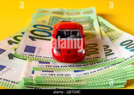 Varna, Bulgarie, 10 mai 2022. Modèle de voiture miniature Porsche rouge sur une pile de 100 billets en euros. Concepts d'assurance automobile et de prêt automobile. Banque D'Images
