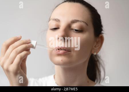 Portrait de la jeune femme aux cheveux foncés prenant un supplément d'huile avec un compte-gouttes en verre. CBD huile de médecine de chanvre appliquée sur la langue Banque D'Images