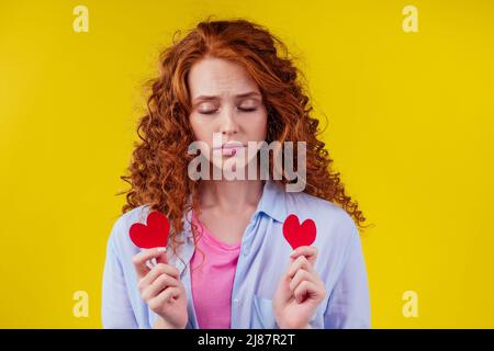 Tristes redhaired Ginger Cry marly femelle déchirant rouge coeur de papier cassé dans le fond jaune studio Banque D'Images